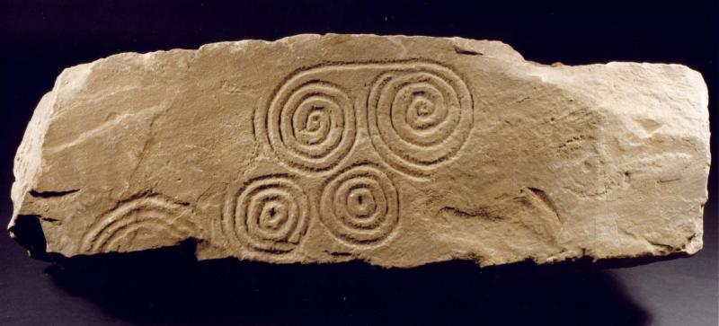 A photograph showing a broken slab decorated with spirals 